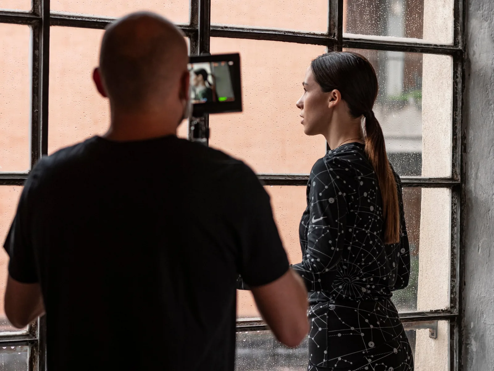 Backstage di un servizio moda: l'operatore riprende una modella davanti a una grande finestra